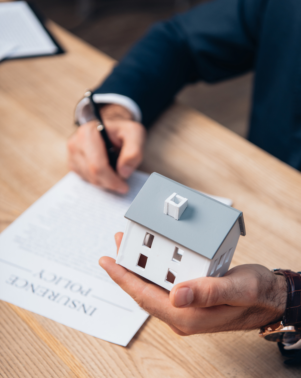 cropped view of lawyer holding house model near documents with insurance policy lettering on table