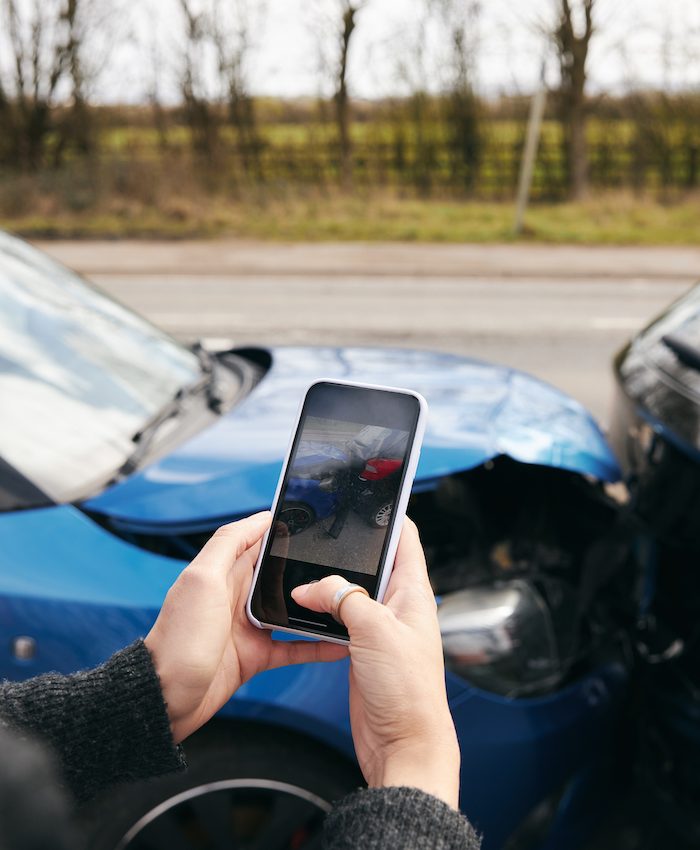 Close up of female driver taking photos of road traffic accident on mobile phone for insurance claim