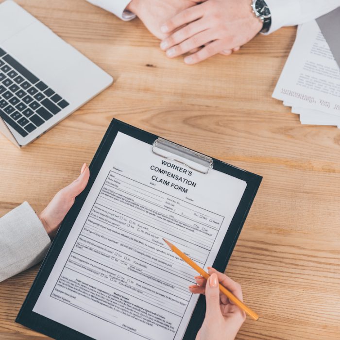 cropped view of businessman sitting at wooden desk while woman filling in compensation claim form