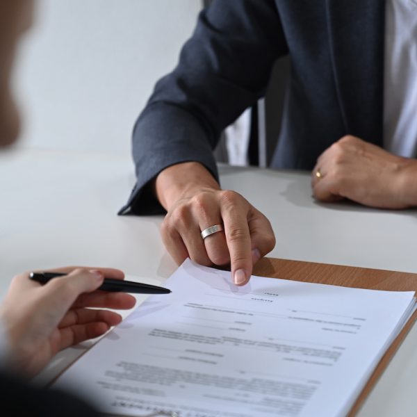 Cropped shot of male lawyer providing law consultation and legal advice to client and showing place for signature on contract document.